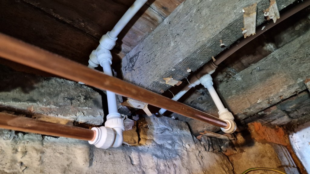 The image depicts a section of copper piping with PVC connectors installed on the wooden beams of a cellar The Best Ways t...