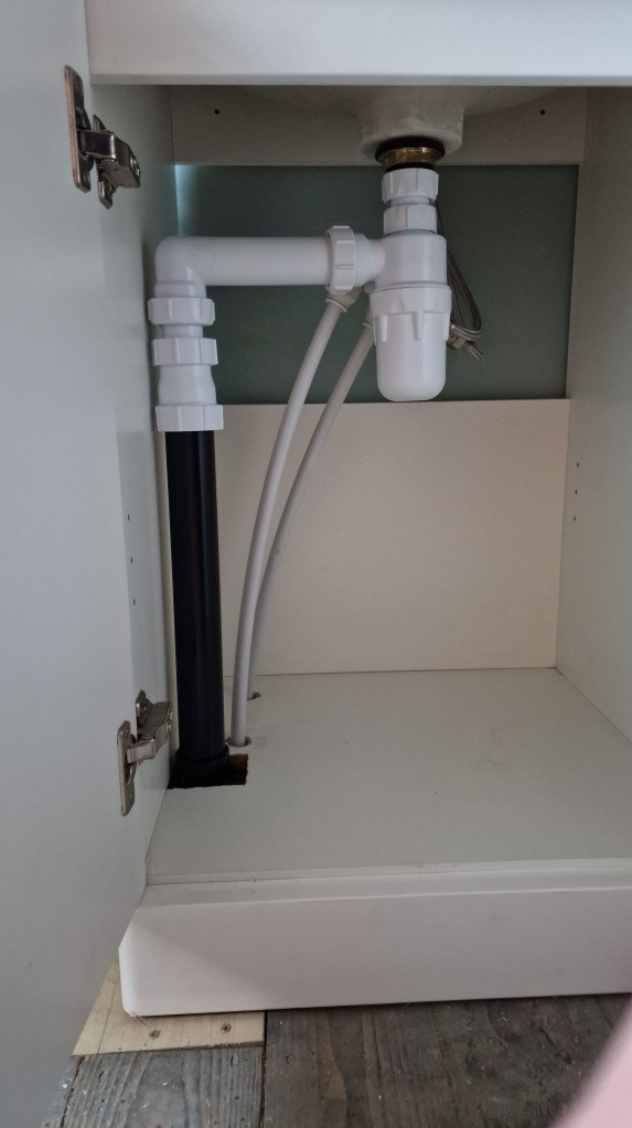The image shows a white cabinet with plumbing installed within it.