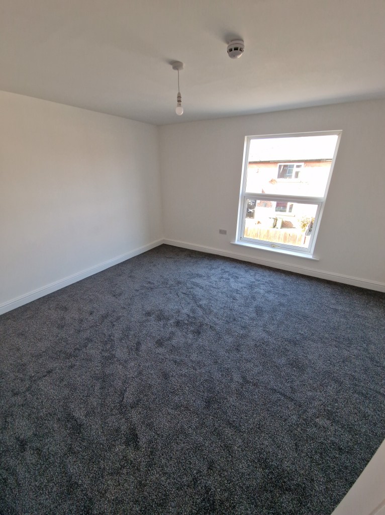 The interior of an unfurnished room with a large window and grey carpeting.