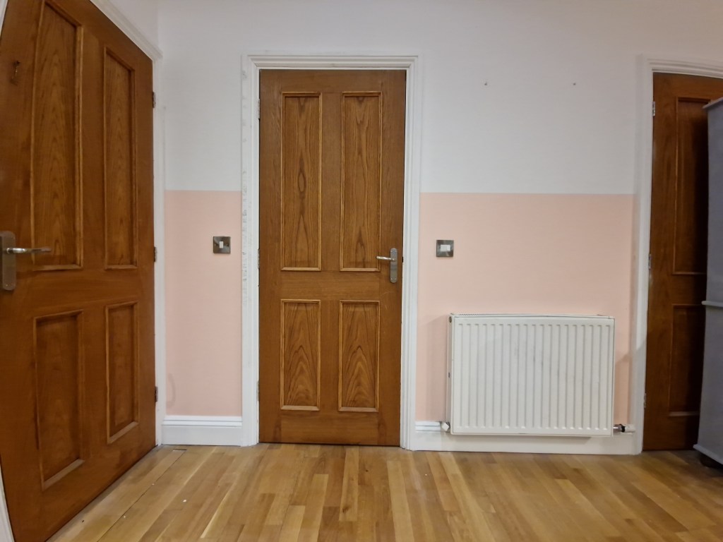There is a closed wooden door towards the center of a room, with paint covered doors to either side and a heating radiator...
