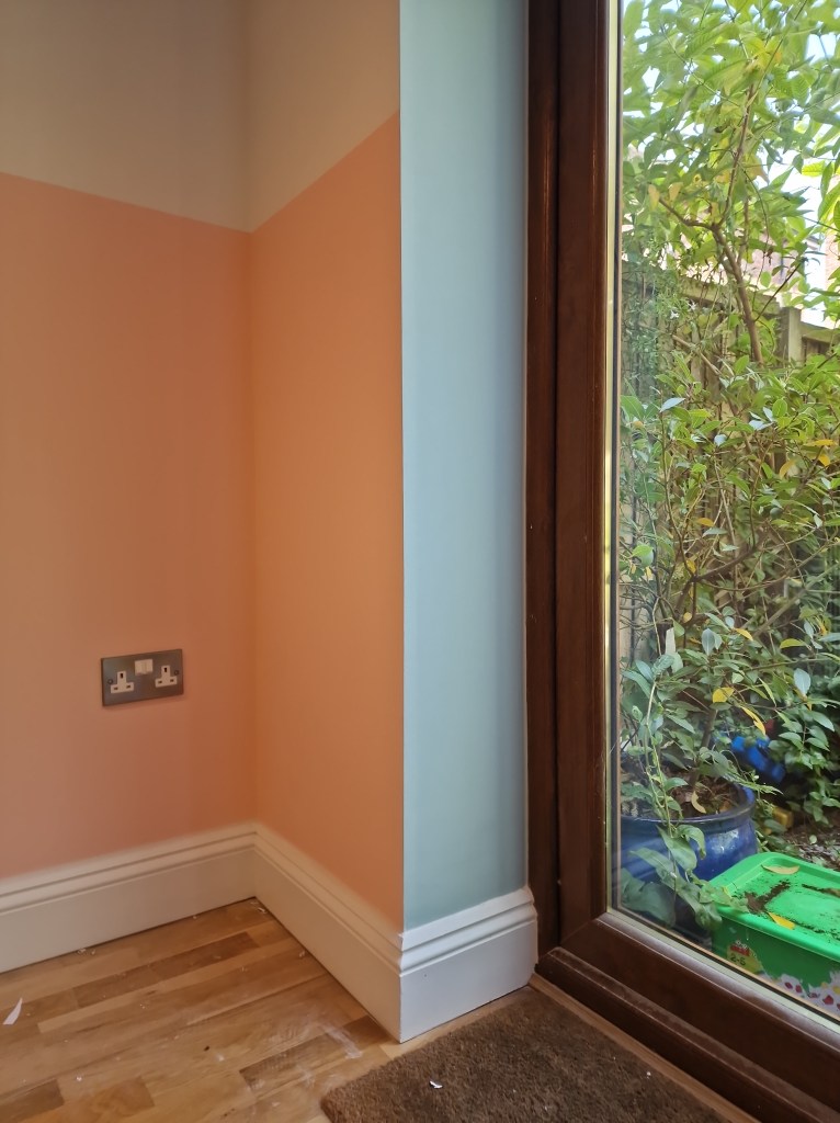 A close-up view of a room's corner, featuring a peach wall and a window with a brown frame, providing a glimpse into the o...