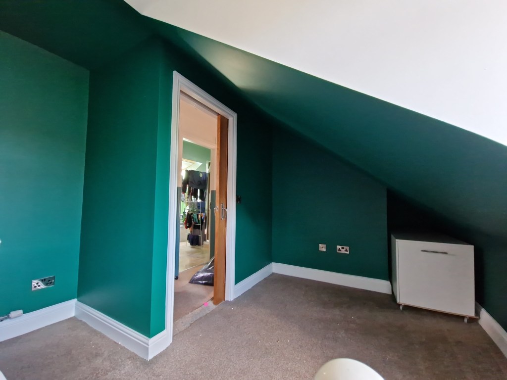 The interior features a teal green wall with crisp white trim, a doorway aligned with the framing of the walls, and a slan...