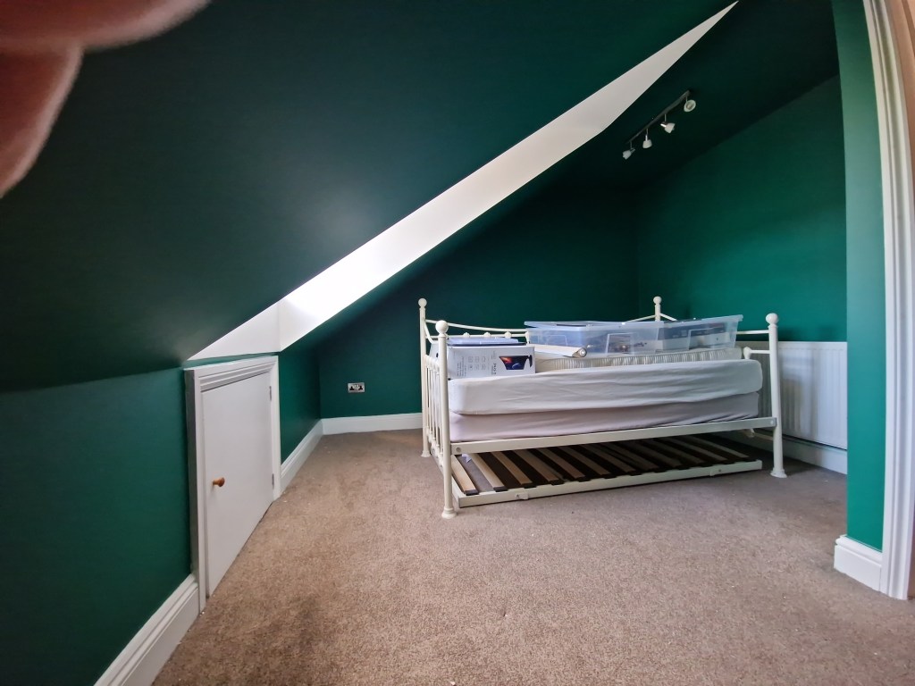 A room with a bed, painted in green and white, featuring a close-up of fingers above.
