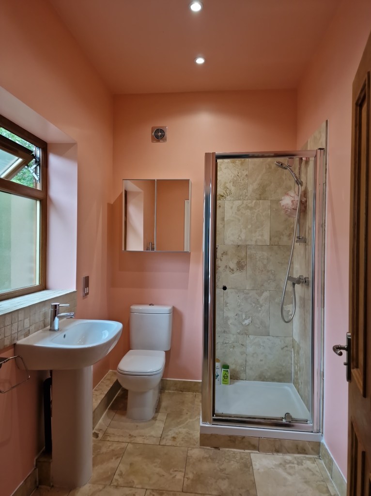 A bathroom with a white sink, white toilet, and glass-enclosed shower. The walls are peach-colored and the floor has large...